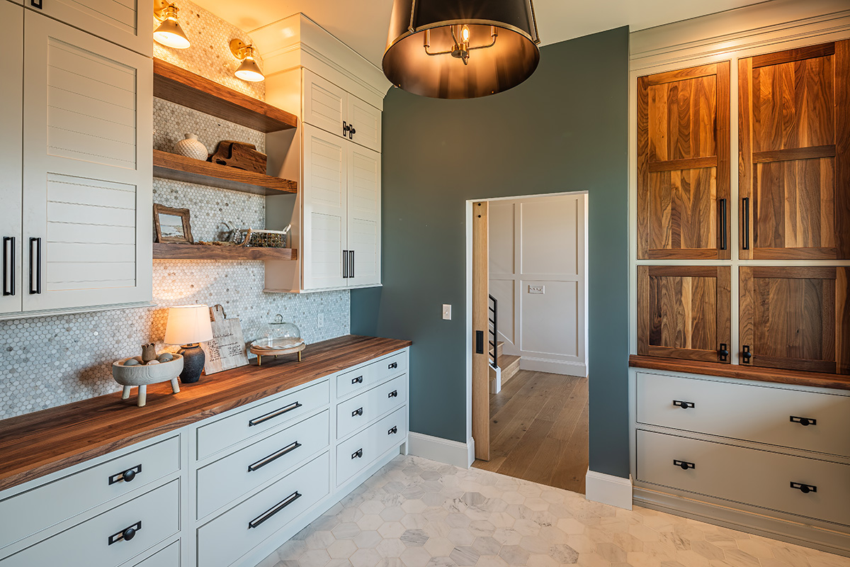 white cabinet storage room with black handles and knobs. White tile flooring and teal wall color. Stone backsplash sits above the wooden countertops.