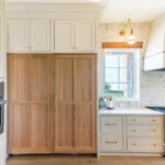 white wood kitchen with gold accents, dark wooden fridge, stainless steel appliances and stone backsplash