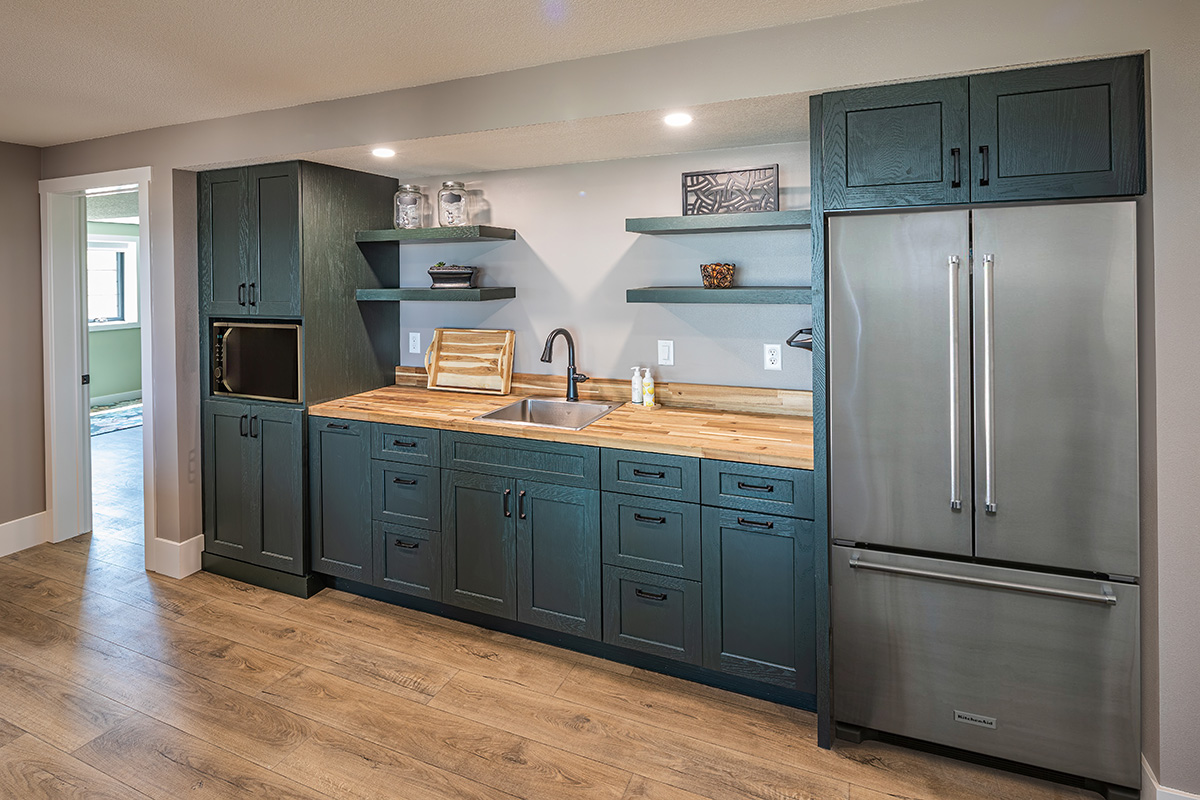 teal wooden cabinetry with stainless steel fridge. Light brown wooden countertops.