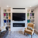White built in cabinets around a built in fireplace along the narrow wall of a living room.