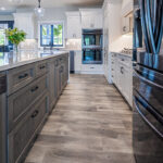 White kitchen cabinetry with black accents. Brushed wooden floor and modern light fixtures.