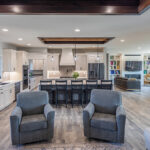 Shows a wide-angle view of the living spaces including a kitchen, dining space, and two sitting areas. The space is cohesive with white cabinets and color scheme.