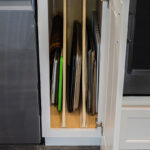 white cutting board cabinet filled with various trays and cutting boards.