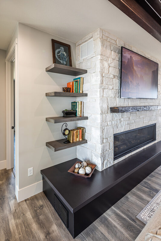electric fireplace surrounded by stone. the attached wooden shelving unit is holding books and pictures.