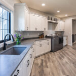 grey countertops with white cabinets. the floor is a brushed grey natural wood. this kitchen shows a layout for built in washer & dryer in the kitchen space.