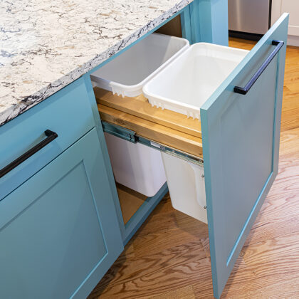 A blue kitchen cabinet with a trash can in it.
