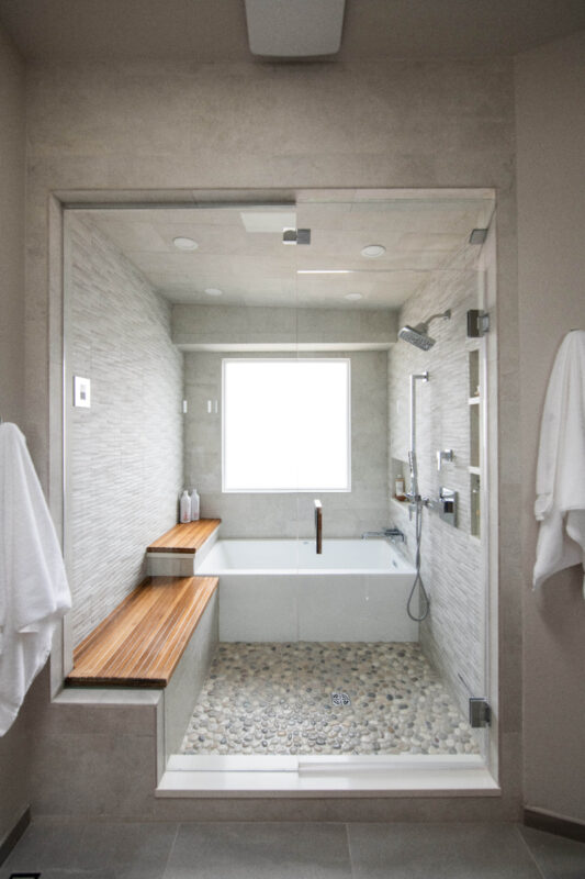 Bathroom shower behind glass with bench seating and tub