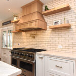 kitchen with stained and painted cabinets. Includes floating shelves and a wood hood above a professional stove