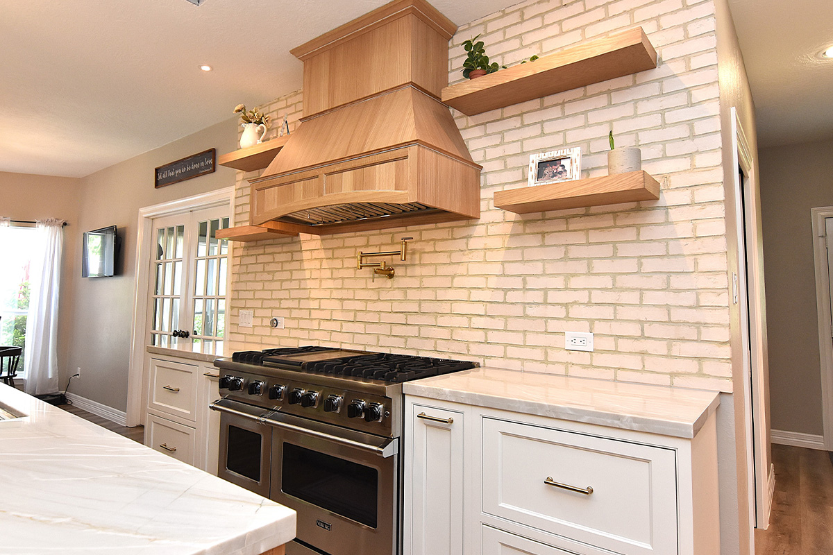 kitchen with stained and painted cabinets. Includes floating shelves and a wood hood above a professional stove