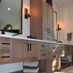 Stained bathroom vanity cabinets with open shelf on the bottom and a countertop wall cabinet splitting 2 sinks