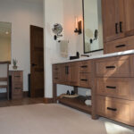 Stained bathroom vanity cabinets with open shelf on the bottom and a countertop wall cabinet splitting 2 sinks