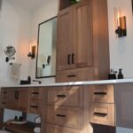 Stained bathroom vanity cabinets with open shelf on the bottom and a countertop wall cabinet splitting 2 sinks