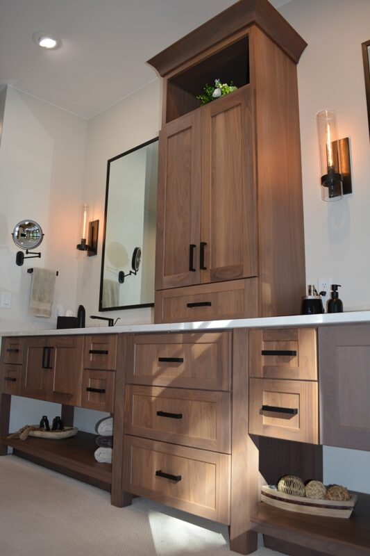 Stained bathroom vanity cabinets with open shelf on the bottom and a countertop wall cabinet splitting 2 sinks