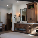 Stained bathroom vanity cabinets with open shelf on the bottom and a countertop wall cabinet splitting 2 sinks