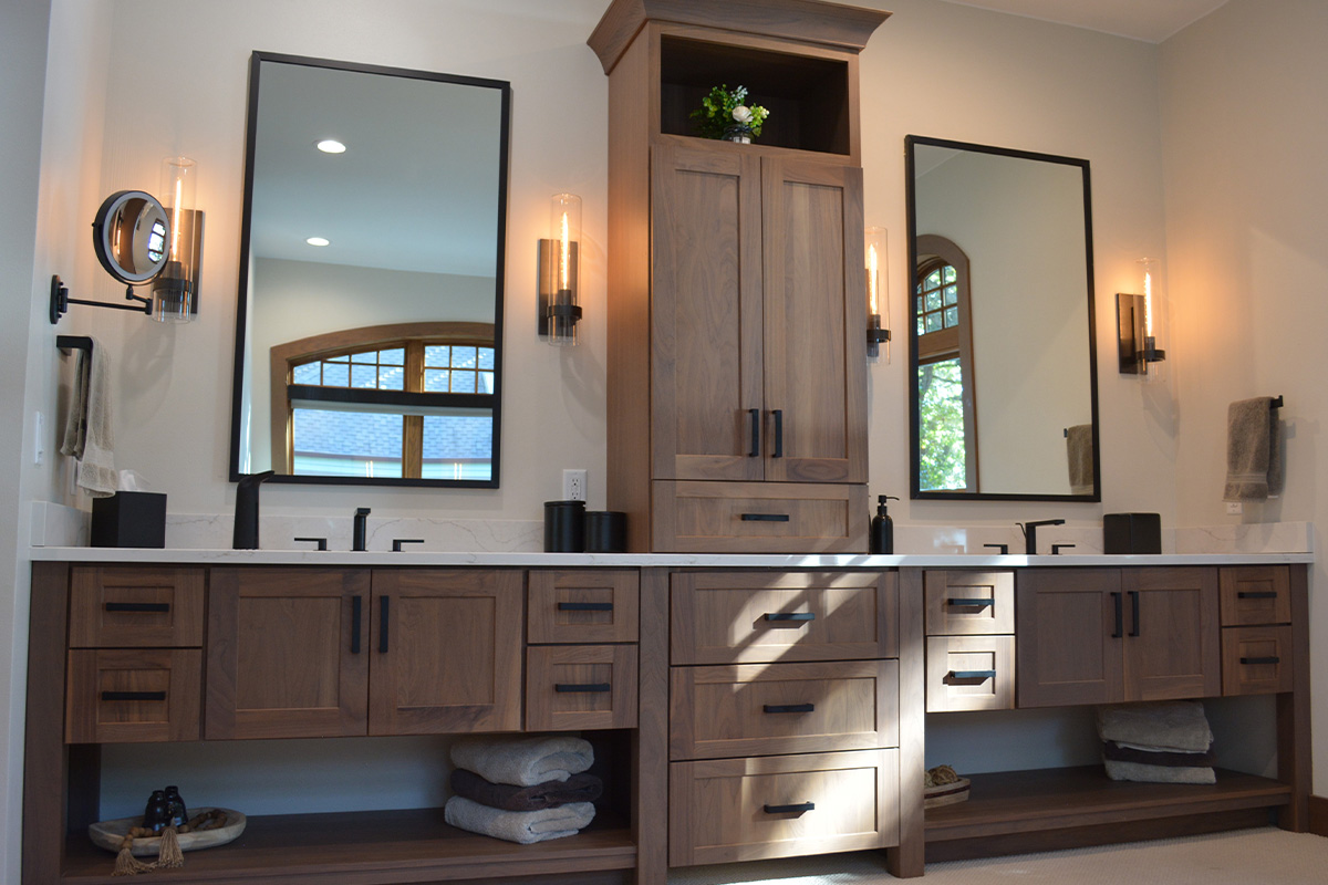 Stained bathroom vanity cabinets with open shelf on the bottom and a countertop wall cabinet splitting 2 sinks