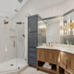 Master bathroom with stained vanity cabinets and painted tall linen cabinets. Also includes a shower with glass walls.