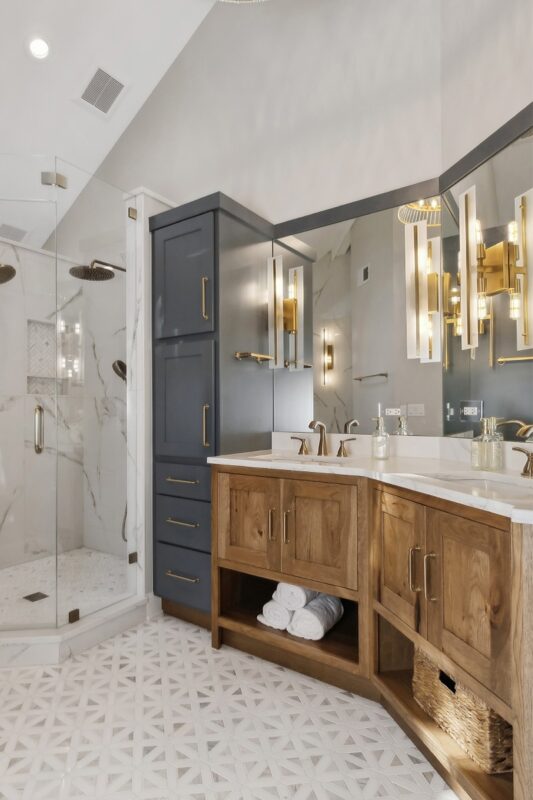 Master bathroom with stained vanity cabinets and painted tall linen cabinets. Also includes a shower with glass walls.