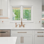 Shows a window above a kitchen sink, surrounded by white painted cabinets