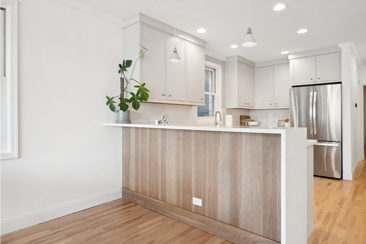 Kitchen peninsula with painted cabinets and a stained wood panel back