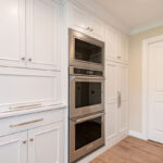 White painted kitchen cabinets with stacked ovens.