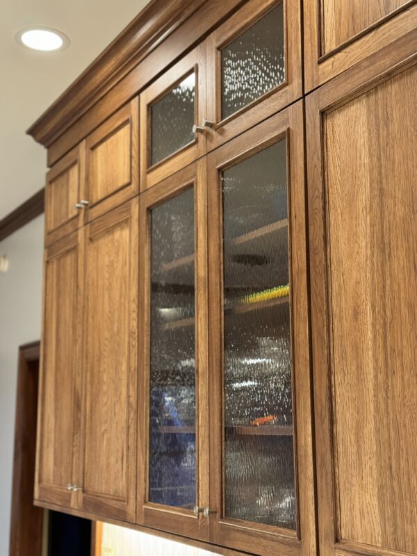 Stained kitchen cabinet. Photo shows detail of the applied molding Savannah door style and glass inserts in 4 doors on a stacked wall cabinet.