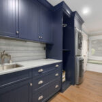 Blue painted laundry room cabinets with a sink and stacked washer/drier.