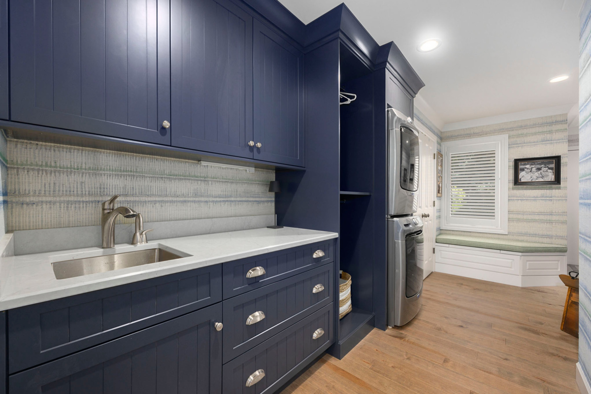 Blue painted laundry room cabinets with a sink and stacked washer/drier.