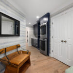 Blue painted laundry room cabinets with a sink and stacked washer/drier and a mudroom space with bench seating area.