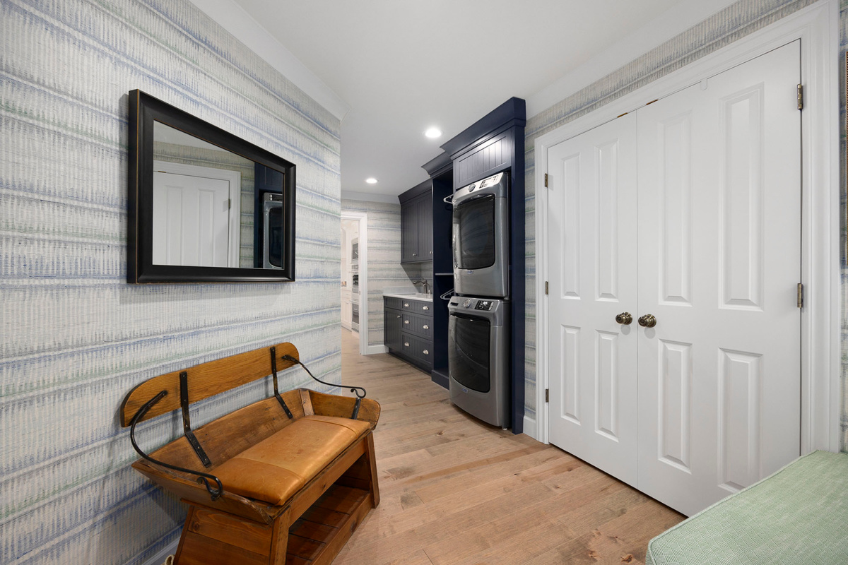 Blue painted laundry room cabinets with a sink and stacked washer/drier and a mudroom space with bench seating area.