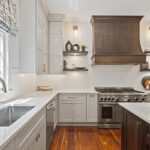 White painted kitchen perimeter cabinets with stained curved wood hood and island.