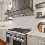 White painted kitchen perimeter cabinets with stained curved wood hood and island.