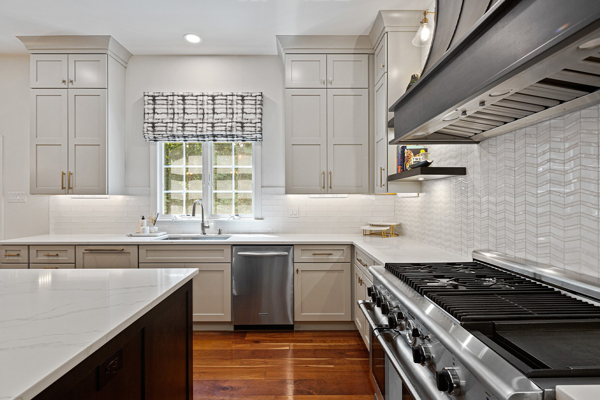 View of a window surrounded by white and stained kitchen cabinets with stainless steel oven.