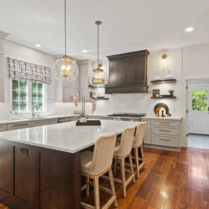 White painted kitchen perimeter cabinets with stained curved wood hood and island.