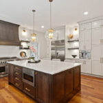 White painted kitchen perimeter cabinets with stained curved wood hood and island.