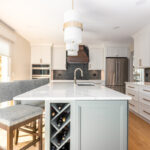 White painted kitchen perimeter with stained wood hood and gray painted island that includes a wine rack cabinet on the side.