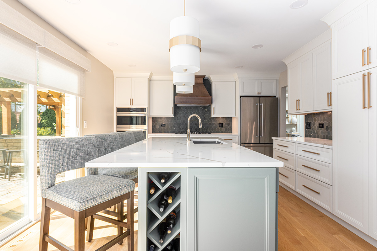 White painted kitchen perimeter with stained wood hood and gray painted island that includes a wine rack cabinet on the side.