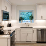 kitchen with white painted perimeter cabinets with view of dishwasher, oven, sink with window.