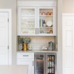 White painted kitchen cabinet with glass doors above a wine fridge