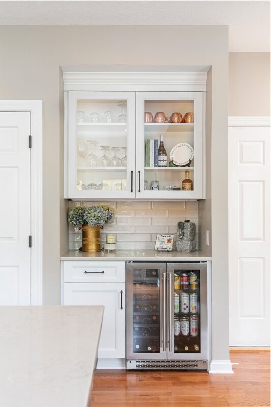 White painted kitchen cabinet with glass doors above a wine fridge