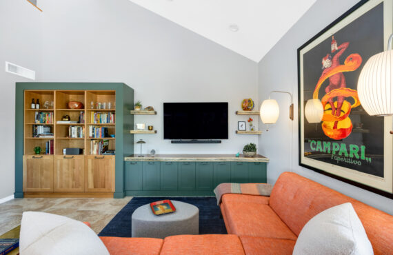 Living room space with painted green cabinets below a tv on the wall and stained white oak book cases to the left framed with green end panels.