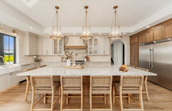 Painted and stained kitchen cabinets in a large open space with large windows.