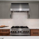 Painted gray and stained brown kitchen cabinets. Showing stove and metal blower above.