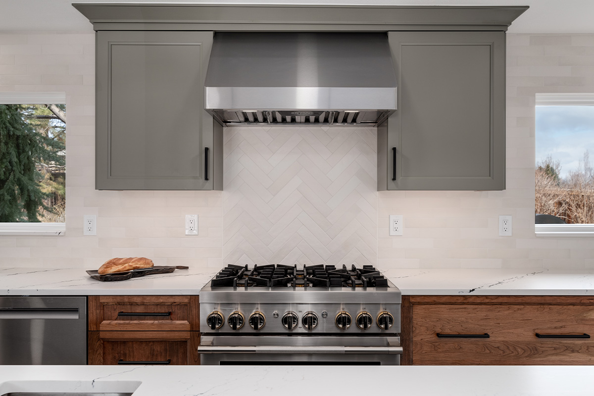 Painted gray and stained brown kitchen cabinets. Showing stove and metal blower above.