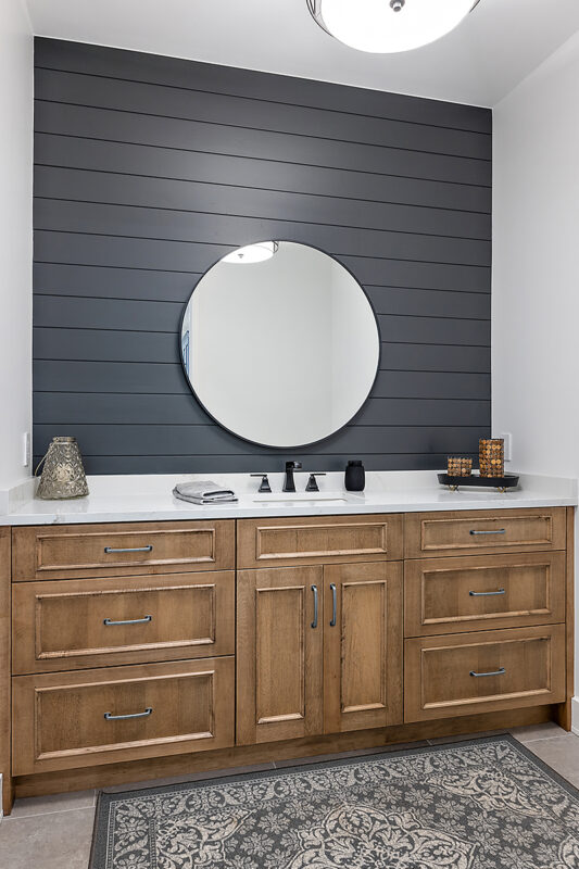 Powder bathroom with brown stained vanity cabinet and a round mirror on a shiplap blue painted wall.