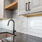 Gun Smoke painted kitchen cabinets with view of sink and tile backsplash