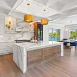 White kitchen cabinets with brown stained island with marble waterfall counter and hood
