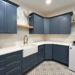 Blue painted laundry room cabinets with white appliances and stained floating shelves