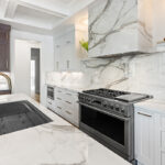 White kitchen cabinets with brown stained island with marble waterfall counter and hood