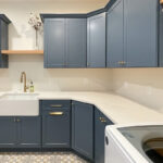 Blue painted laundry room cabinets with white appliances and stained floating shelves