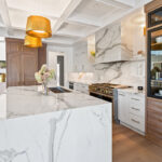 White kitchen cabinets with brown stained island with marble waterfall counter and hood
